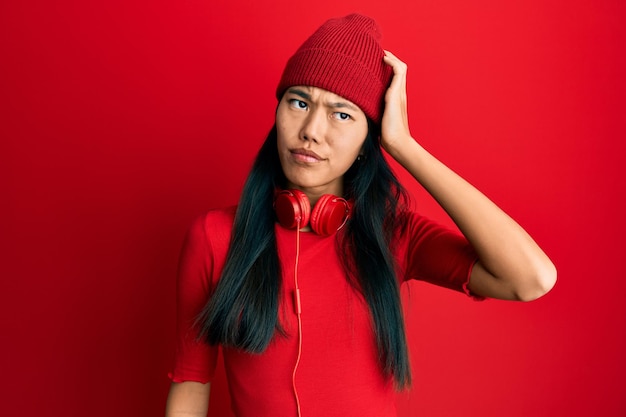 Młoda chinka słuchająca muzyki przez słuchawki myli się i zastanawia się nad pytaniem niepewnym z wątpliwościami myśląc z ręką na głowie zamyślona koncepcja