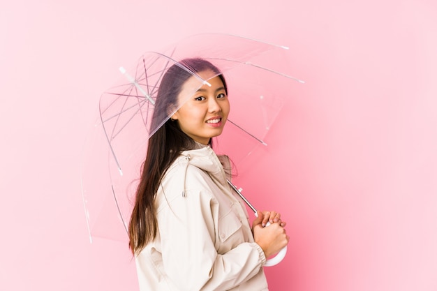 Młoda Chinka trzyma parasol na białym tle wygląda uśmiechnięty, wesoły i przyjemny.