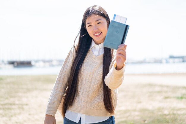 Młoda Chinka trzyma paszport na zewnątrz z radosnym wyrazem twarzy