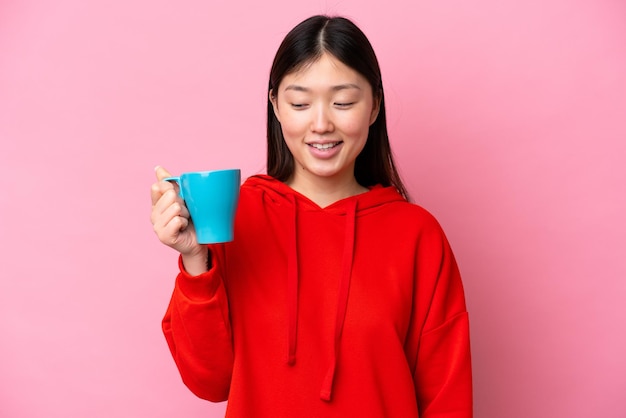 Młoda Chinka trzymająca filiżankę kawy na białym tle na różowym tle ze szczęśliwym wyrazem twarzy