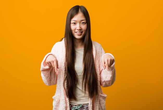 Młoda Chinka w piżamie wskazuje palcami, pozytywne uczucie.