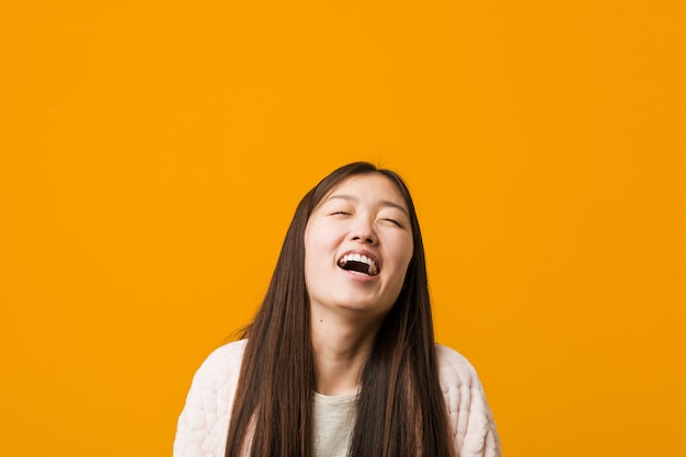 Młoda Chinka w piżamie zrelaksowany i szczęśliwy, śmiejąc się, szyja pokazując zęby.