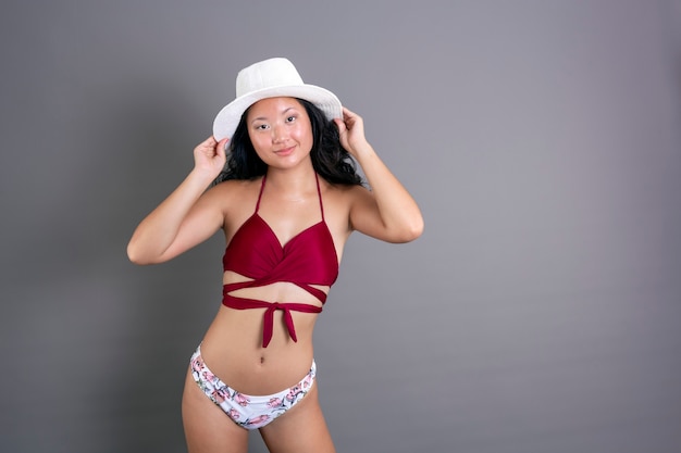 Młoda chińska dziewczyna w bikini w kapeluszu, patrząc w kamerę z nieśmiałym uśmiechem