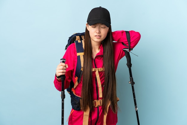 Zdjęcie młoda chińska dziewczyna z plecakiem i kijkami trekkingowymi nad odosobnioną niebieską ścianą z bólem szyi