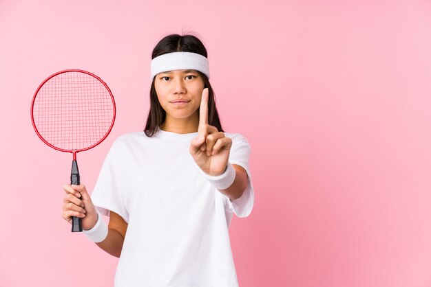 Młoda Chińska Kobieta Bawić Się Badminton W Różowej ścianie Pokazuje Liczbę Jeden Z Palcem.