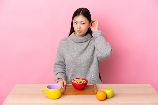 Młoda Chińska kobieta ma śniadanie w stole ma wątpliwości
