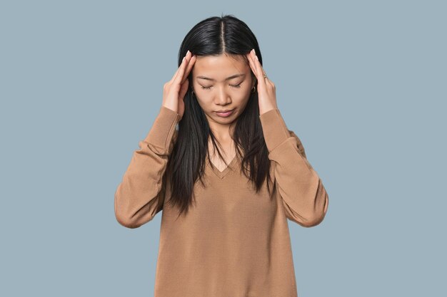 Młoda chińska kobieta w studiu dotykająca świątyń i mająca ból głowy