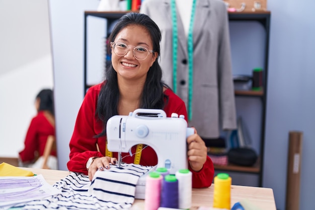 Młoda chińska krawcowa uśmiecha się pewnie za pomocą maszyny do szycia w atelier