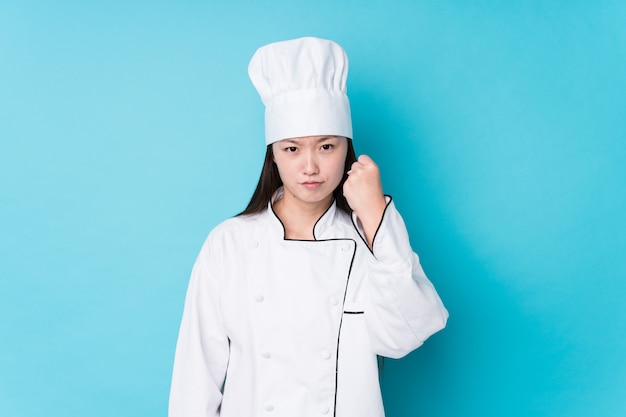 Młoda chińska szef kuchni kobieta odizolowywał pokazywać pięść z agresywnym wyrazem twarzy.