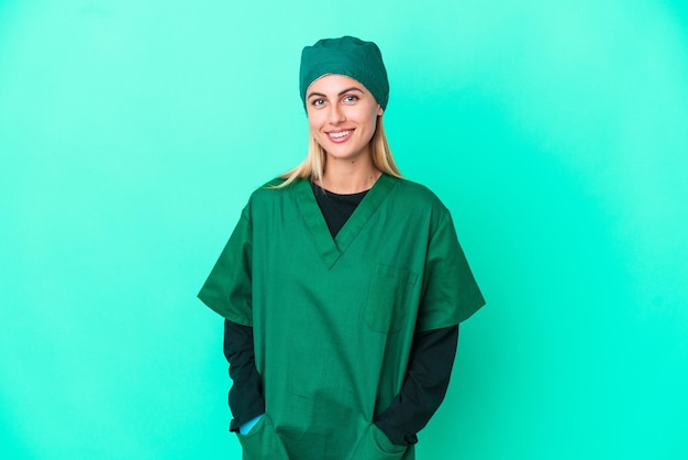 Młoda chirurg urugwajska kobieta w zielonym mundurze na białym tle na niebieskim tle, trzymając ręce skrzyżowane w pozycji czołowej