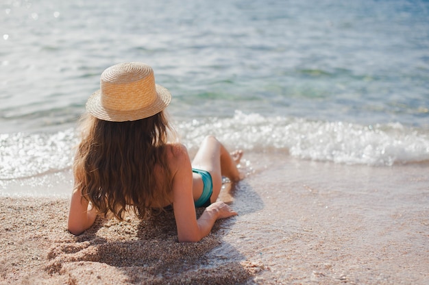 Młoda chuda dama w kapeluszu leżąc na plaży na żółtym piasku w pobliżu fali morza. Widok z góry piękna dziewczyna