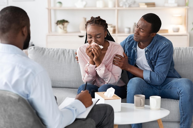 Młoda czarna kobieta płacze na spotkaniu z doradcą rodzinnym, troskliwy mąż pocieszający ją podczas sesji psychoterapii dla par, zdenerwowana afroamerykanka mająca załamanie emocjonalne, wolna przestrzeń