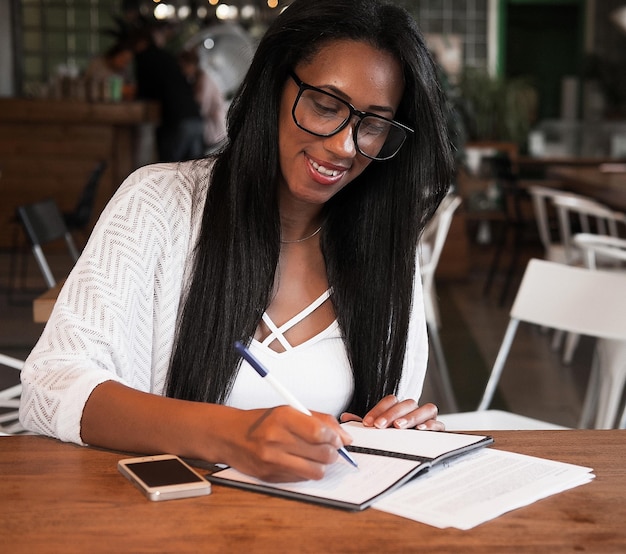Młoda czarna kobieta siedzi w kawiarni i pisze notatki koncepcja stylu życia