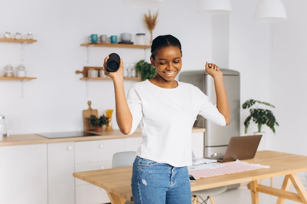 Młoda czarna kobieta tańczy w kuchni trzymając głośnik bluetooth