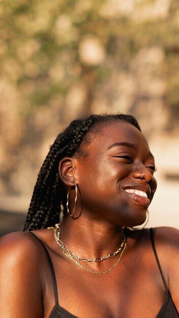 Młoda czarna kobieta z warkoczami we włosach i kolczykami uśmiecha się szczęśliwie.
