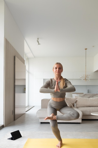 Młoda dama ćwiczy jogę w domu z komputerem typu tablet