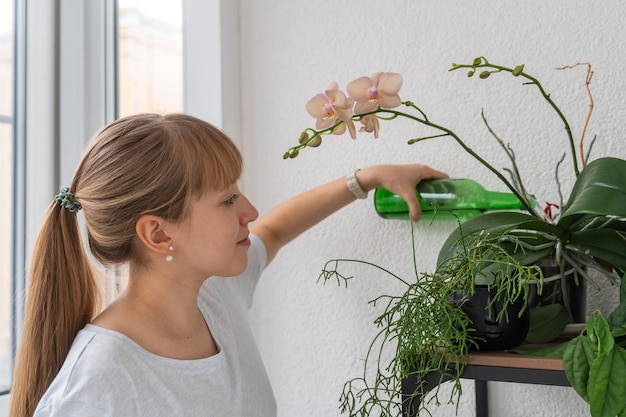 Młoda dama podlewanie orchidei z plastikową butelką na balkonie w domu gadrening