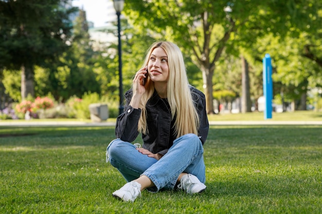 Młoda dama siedzi w parku i rozmawia przez telefon