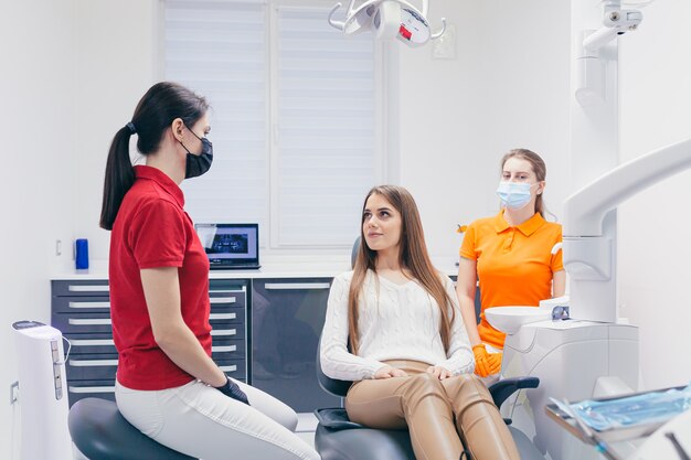 Młoda dentystka rozmawia z pacjentem przed rozpoczęciem leczenia lub zabiegu w nowoczesnej klinice stomatologicznej