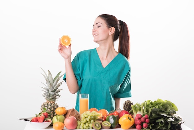 młoda dietetyczka siedząca przy biurku i pokazująca kolorowe warzywa i owoce