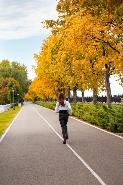 Młoda dorosła kobieta biegająca w jesiennym lesie dziewczyna jogging na drodze