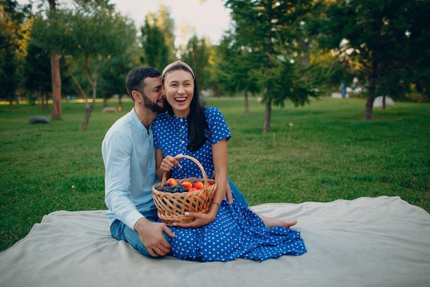 Młoda dorosła kobieta i mężczyzna para piknik siedzi z koszem owoców na łące zielonej trawie w parku.