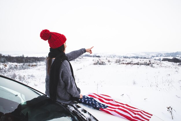 Młoda dorosła kobieta podróżnik siedząca na masce samochodu suv z flagą usa