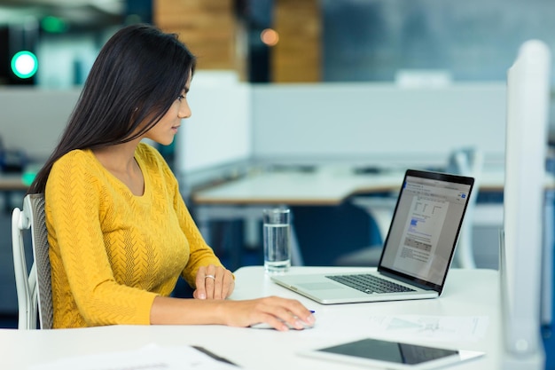 Młoda dorywcza bizneswoman korzystająca z laptopa w biurze