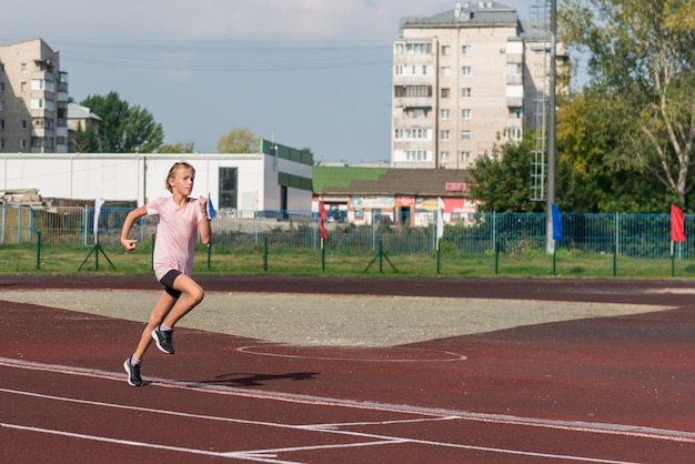 Młoda dziewczyna biegająca po bieżni na stadionie na świeżym powietrzu