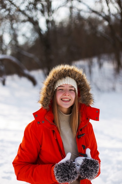 Młoda dziewczyna, blondynka, w swetrze, czapce i pomarańczowej kurtce, na tle zimowego krajobrazu. Śnieg i mróz, koncepcja Bożego Narodzenia.