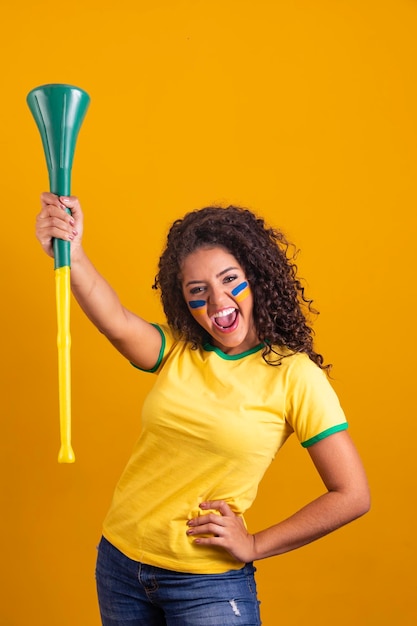 Młoda dziewczyna brazylijska cheerleaderka z wuwuzeli na żółtym tle świętuje