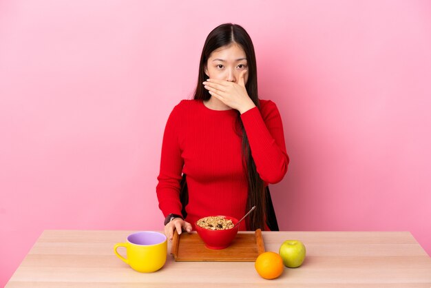 Młoda dziewczyna chiński o śniadanie w tabeli obejmujące usta ręką