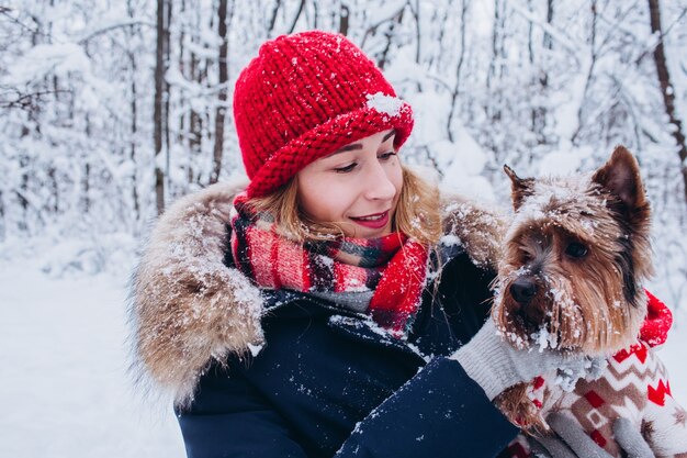 Młoda dziewczyna chodzi zimą po dolnym lesie z psem w świątecznym swetrze