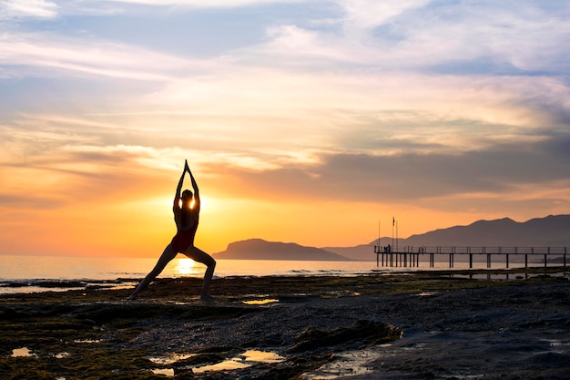 Młoda dziewczyna ćwiczy jogę na plaży podczas zachodu słońca