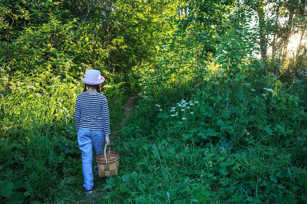 Młoda dziewczyna idąc ścieżką przez zielone lasy niosąc kosz brzozowy