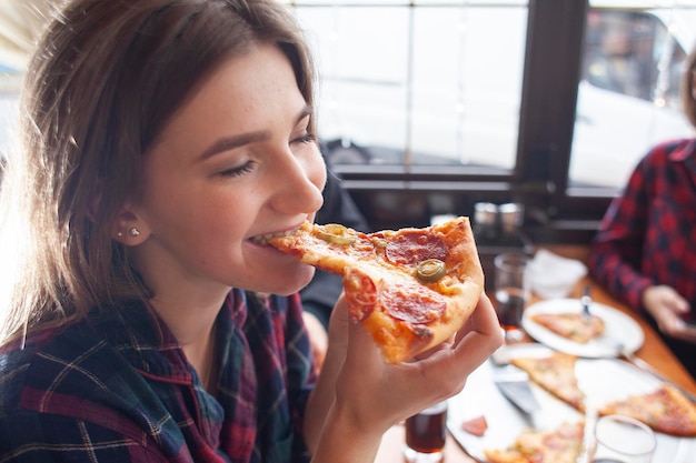 Młoda dziewczyna je kawałek pizzy w pomieszczeniu dziewczyna student daje zbliżenie pizzy