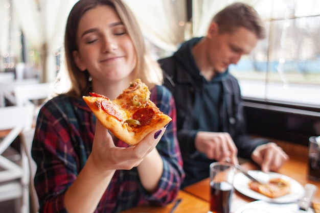 Młoda dziewczyna je plasterek pizzę indoors