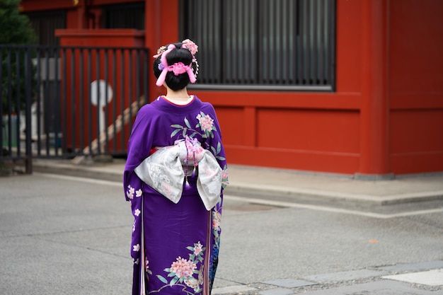 Młoda dziewczyna jest ubranym Japońską kimonową pozycję przed Sensoji świątynią w Tokio, Japonia.