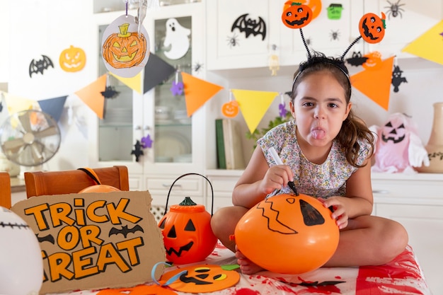 Młoda dziewczyna kaukaski wystaje język podczas malowania czaszki na balonie. Koncepcja przygotowań do obchodów Halloween.