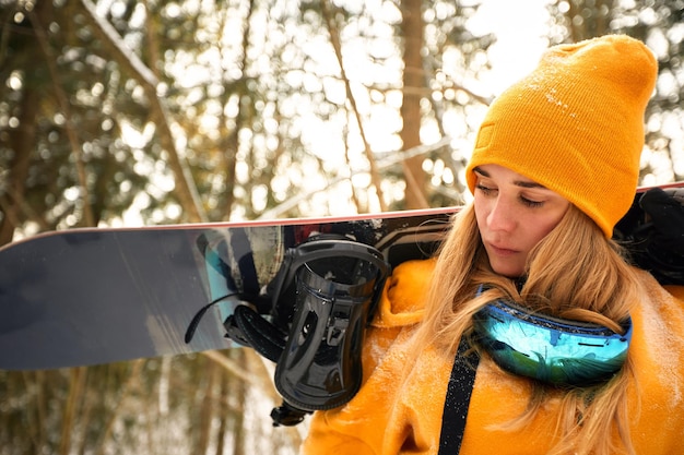 Zdjęcie młoda dziewczyna lub kobieta snowboardzistka idzie na sporty zimowe w zaśnieżonym lesie, stoi na śniegu i trzyma snowboard