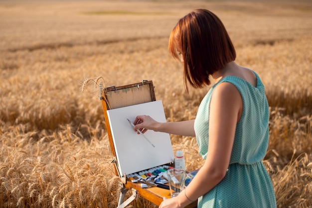 Młoda dziewczyna maluje krajobraz pola żyta o zachodzie słońca