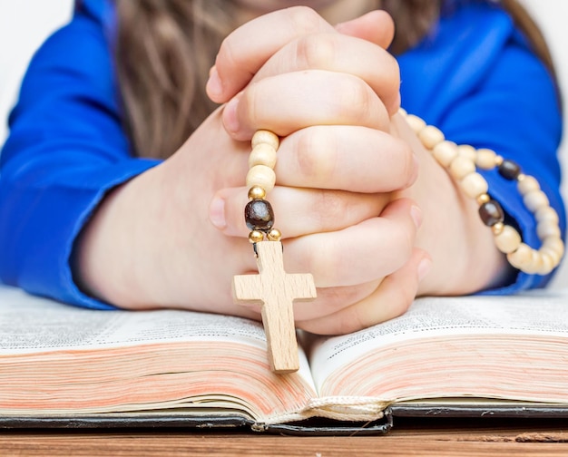 Młoda dziewczyna modli się nad otwartą Biblią, trzymając w dłoni różaniec