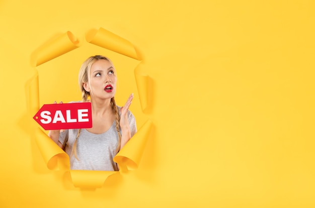 Zdjęcie młoda dziewczyna myśli z napisem sprzedaży na rozdartej żółtej powierzchni