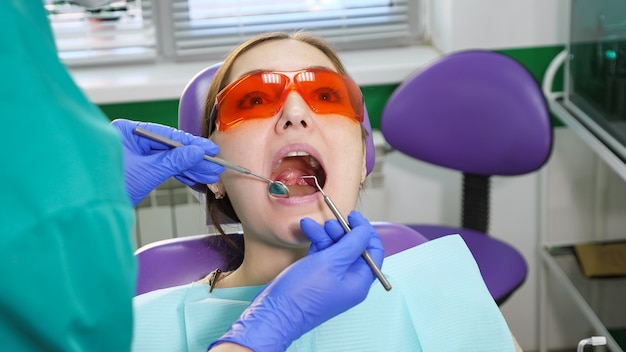 Młoda dziewczyna na badania profilaktyczne w fotelu dentystycznym u dentysty. Ręce stomatologa z narzędziami dentystycznymi sprawdzają uzębienie pacjenta. Koncepcja pielęgnacji zębów.