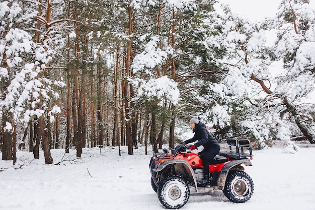 Młoda dziewczyna na motocyklu jedzie w śnieżystym sosnowym lesie w zimie