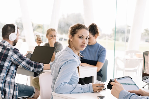 Młoda dziewczyna odwróciła się przed stołem z innymi ludźmi pracującymi w coworkingu