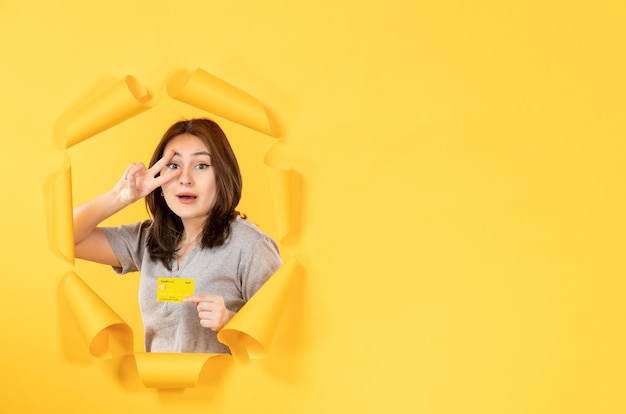 młoda dziewczyna patrząca przez dziurę z kartą kredytową w żółtym tle pieniądze z okna