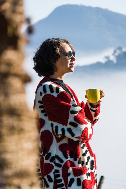 młoda dziewczyna pijąca kawę z kubka w zimny dzień za dużo mgły i chmur zasłania widok na miasto