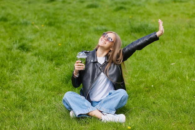 Młoda dziewczyna pije orzeźwiający koktajl z lodem na zielonej trawie