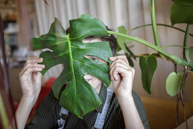 Zdjęcie młoda dziewczyna pokrywa twarz zielonymi liśćmi dla zabawy i relaksu rośliny domowe na balkonie gen z